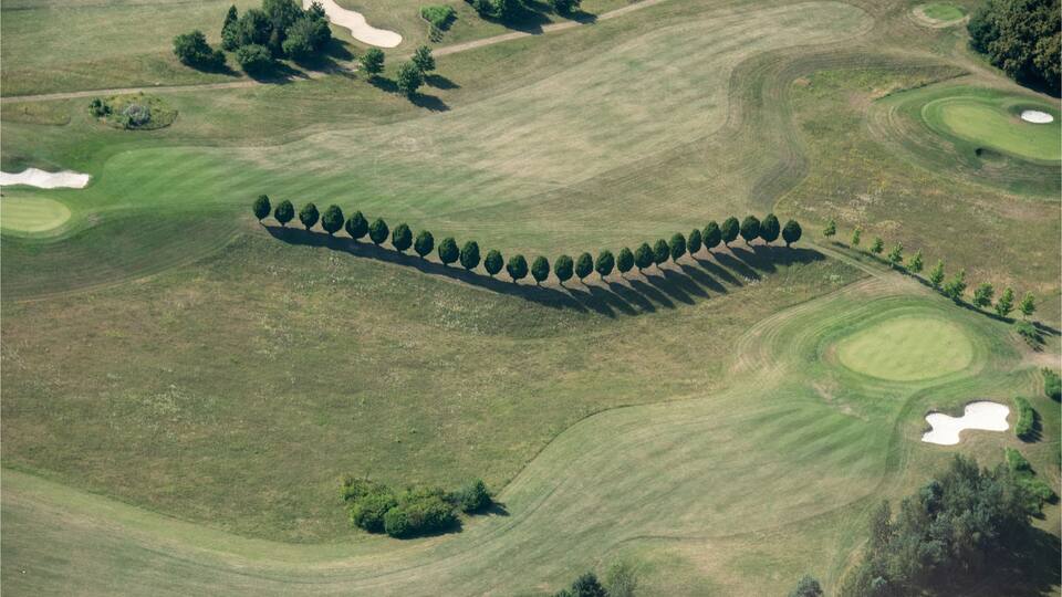 An aerial view of a golf course with sand bunkers, water hazards, and a row of trees along the fairway.