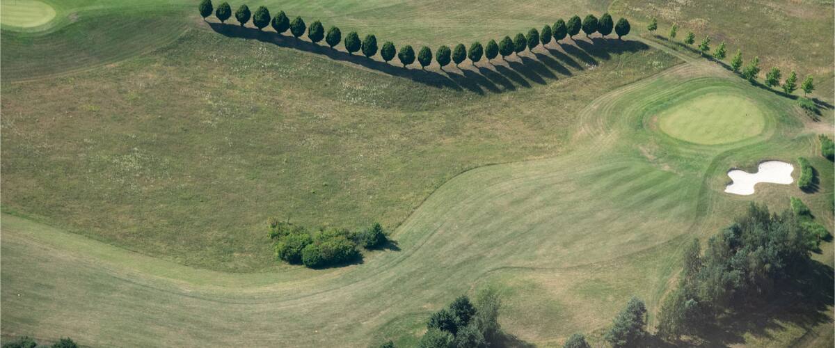 An aerial view of a golf course with sand bunkers, water hazards, and a row of trees along the fairway.