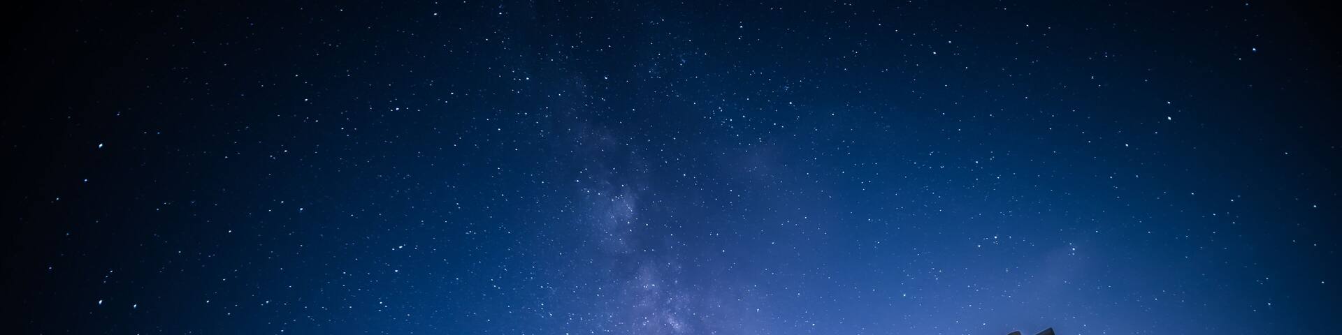 A wooden swing set on a beach at night with a starry sky.