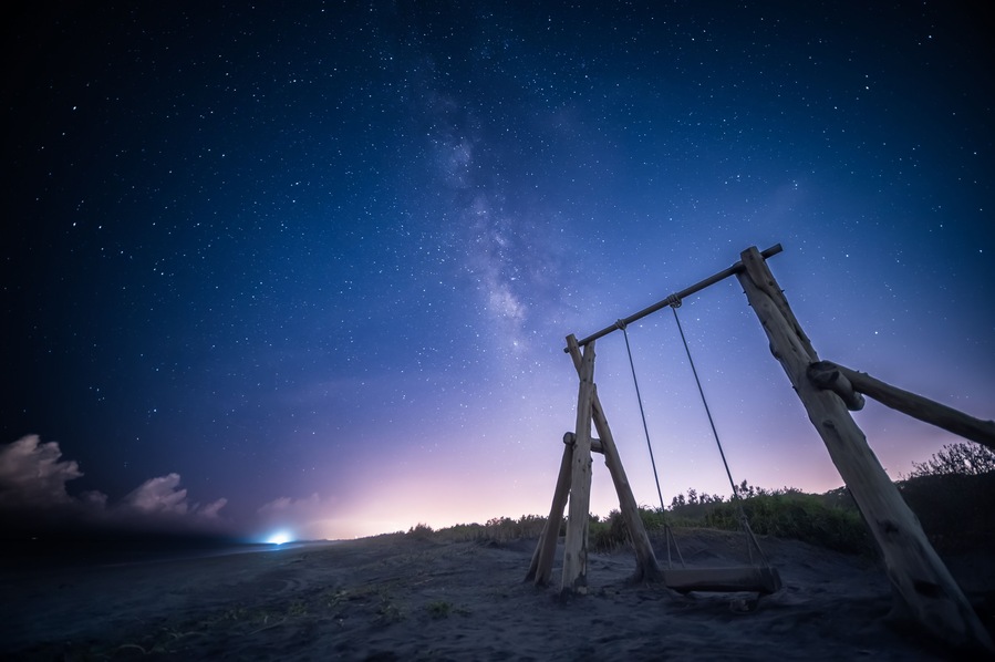 En gungställning i trä på en strand en natt, med en stjärnklar himmel.