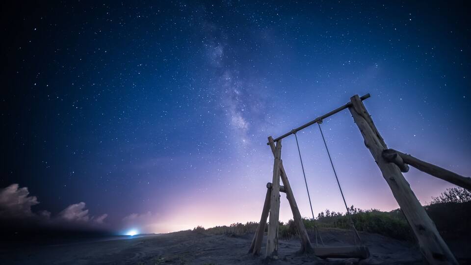 A wooden swing set on a beach at night with a starry sky.