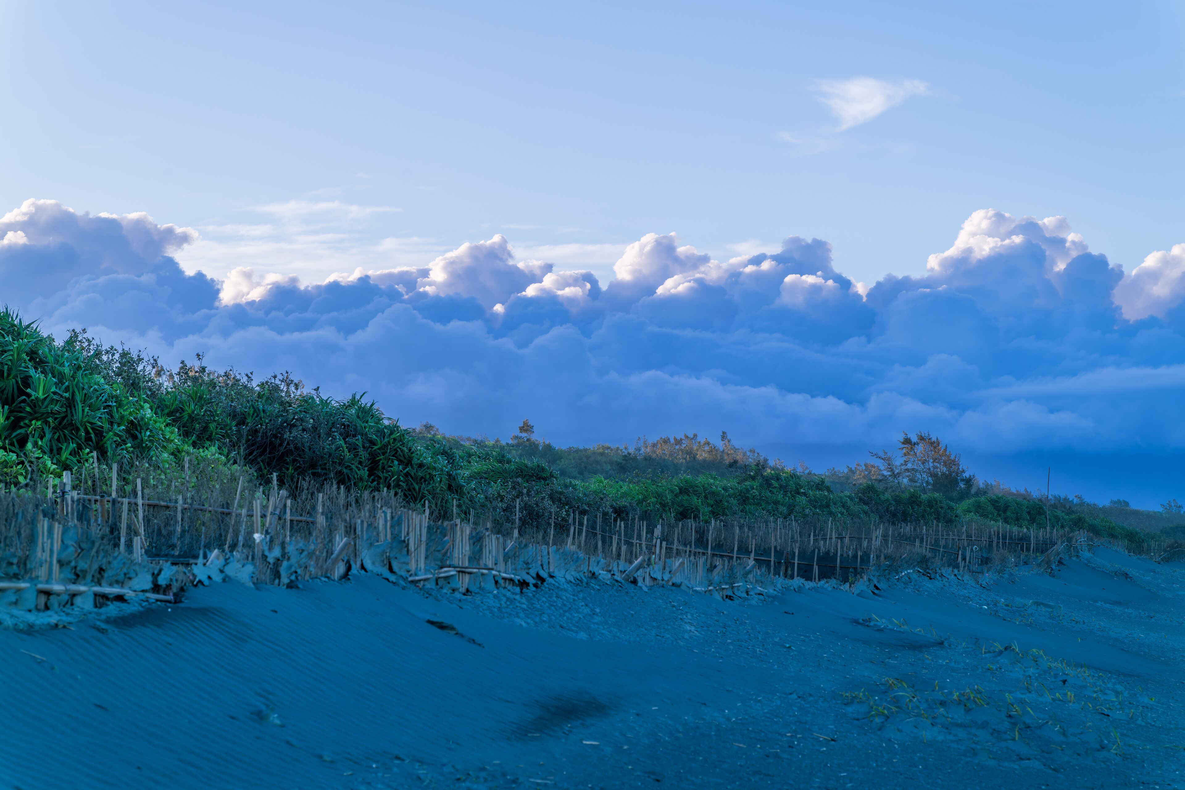 A tranquil beach stretches towards a dramatic sky, where a massive cloud formation dominates the horizon. Zhuangwei Township, Yilan County, Taiwan.
