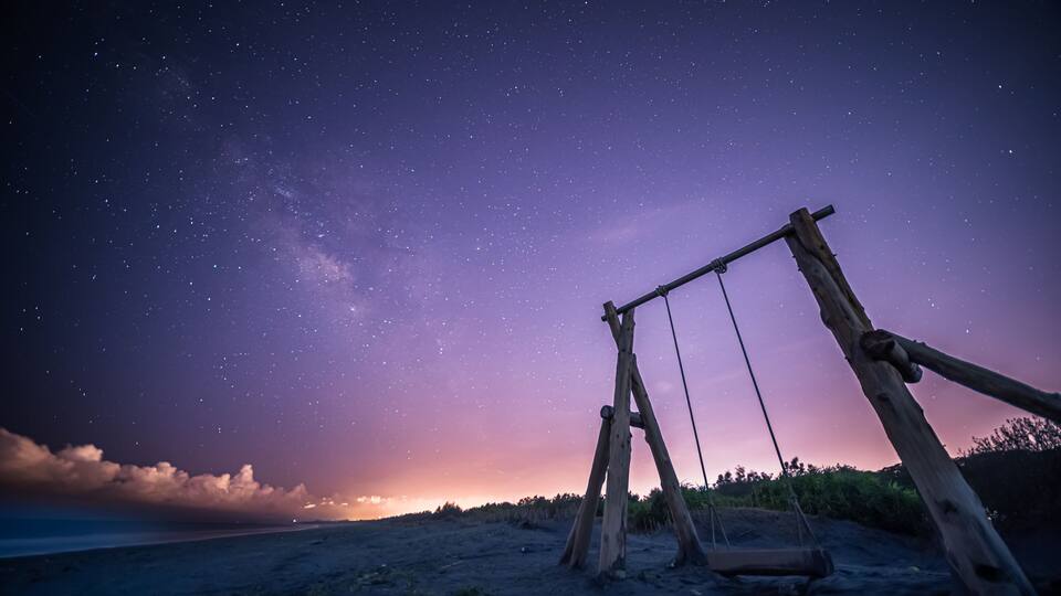 A wooden swing set on a beach at night with a starry sky.