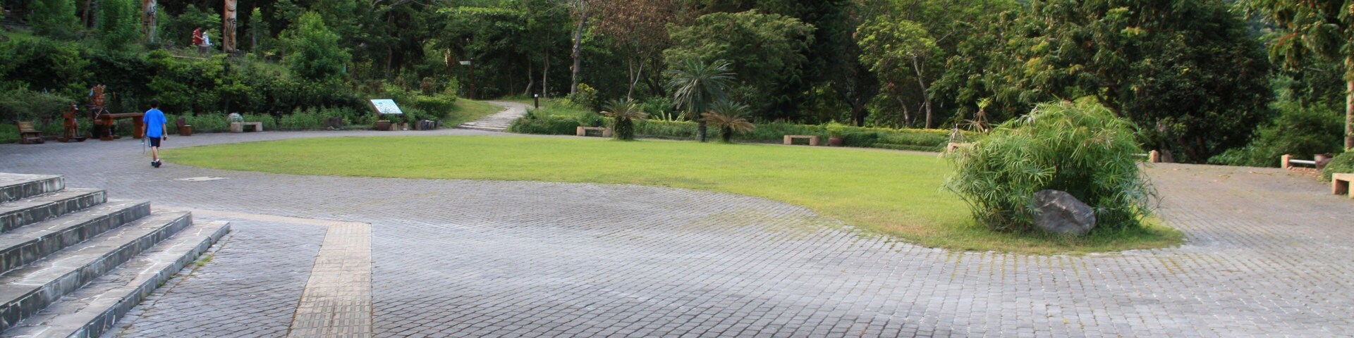 Um caminho pavimentado serpenteia por um parque com área gramada e árvores.