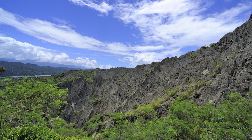 Un paysage montagneux, avec une végétation luxuriante et un ciel bleu clair parsemé de quelques nuages.