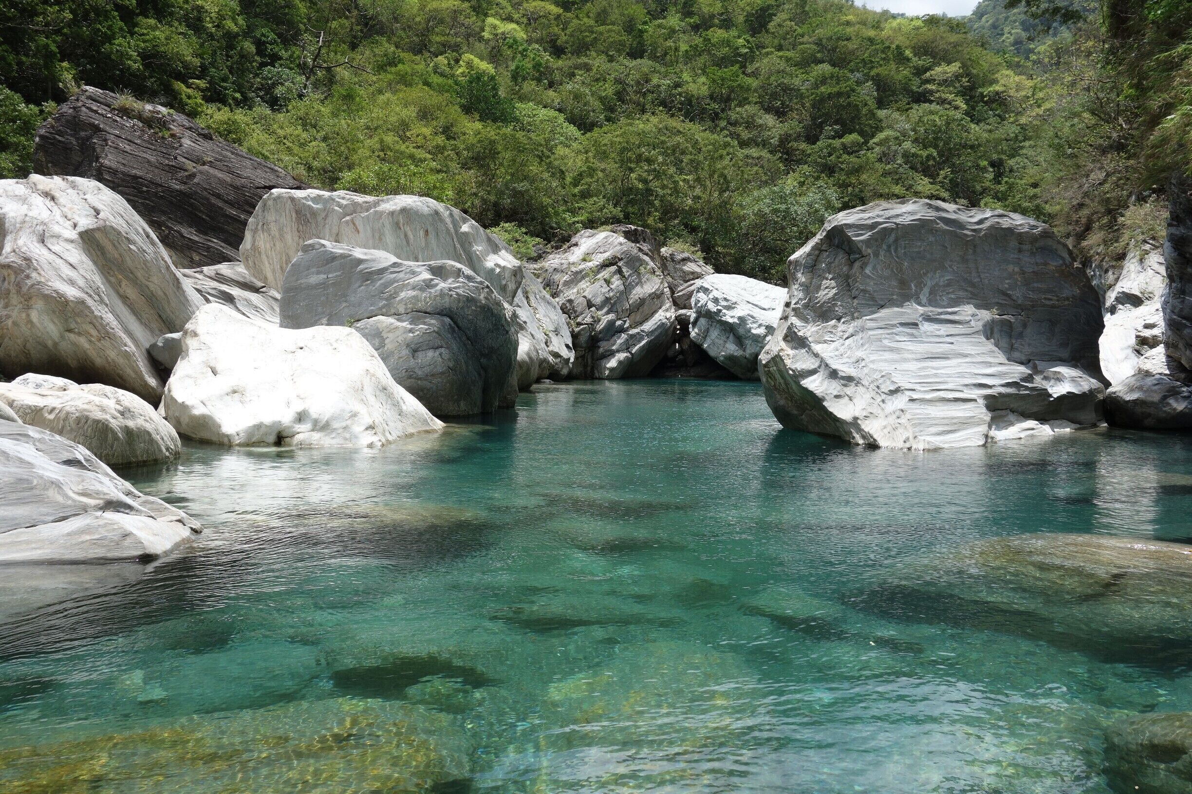 A clear turquoise river surrounded by large white rocks and dense green forest.