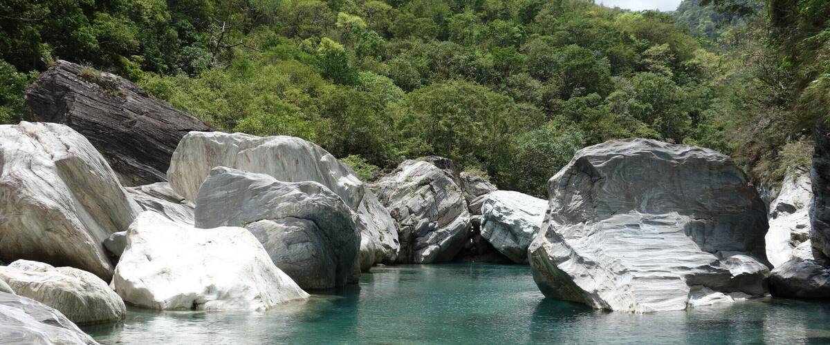 A clear turquoise river surrounded by large white rocks and dense green forest.