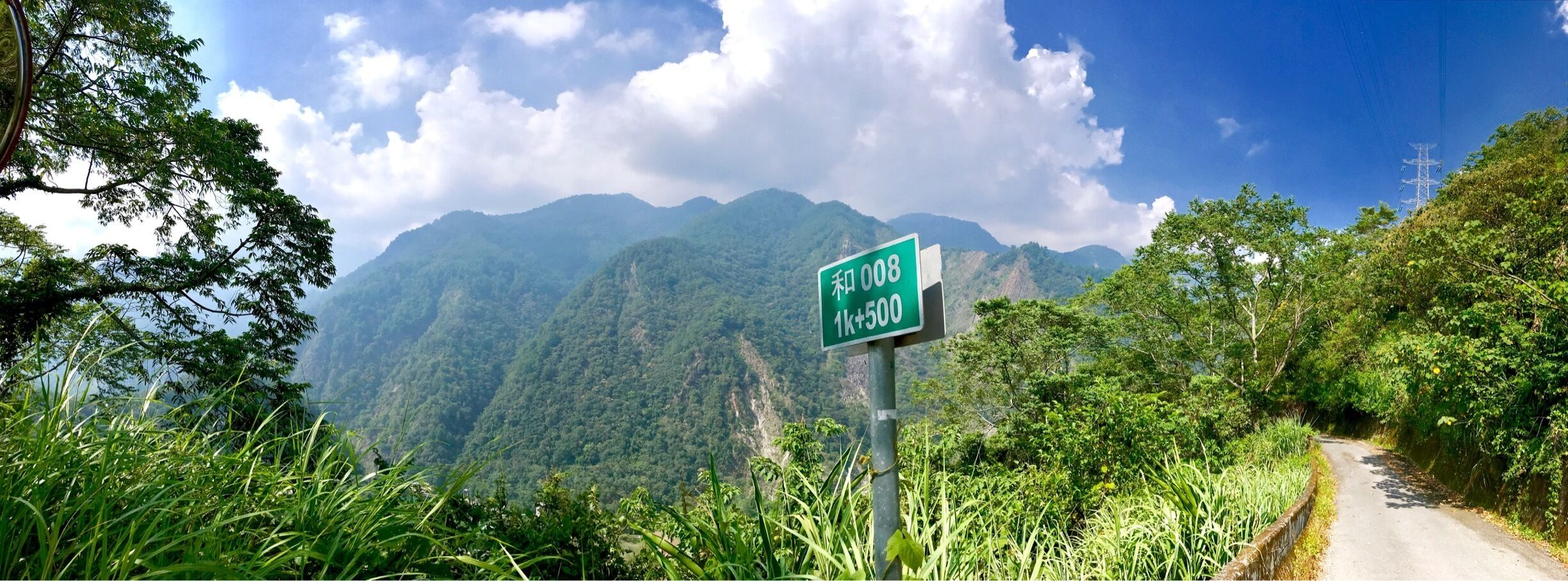 A road sign with '和008 1k+500' on a mountain road surrounded by lush greenery.