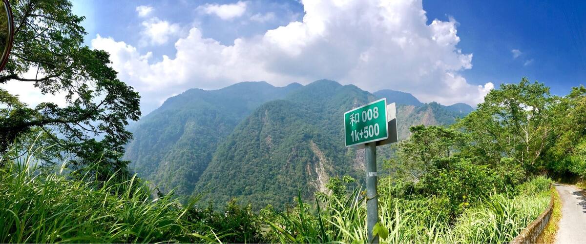 A road sign with '和008 1k+500' on a mountain road surrounded by lush greenery.