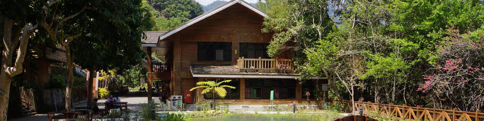 A wooden house with a balcony, a wooden bridge, and a pond.