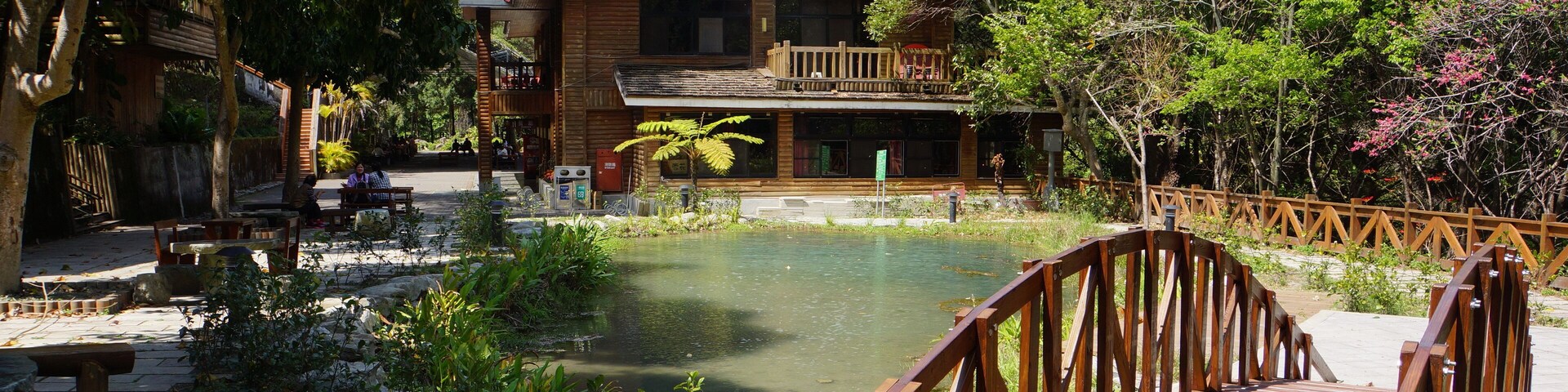 A wooden house with a balcony, a wooden bridge, and a pond.