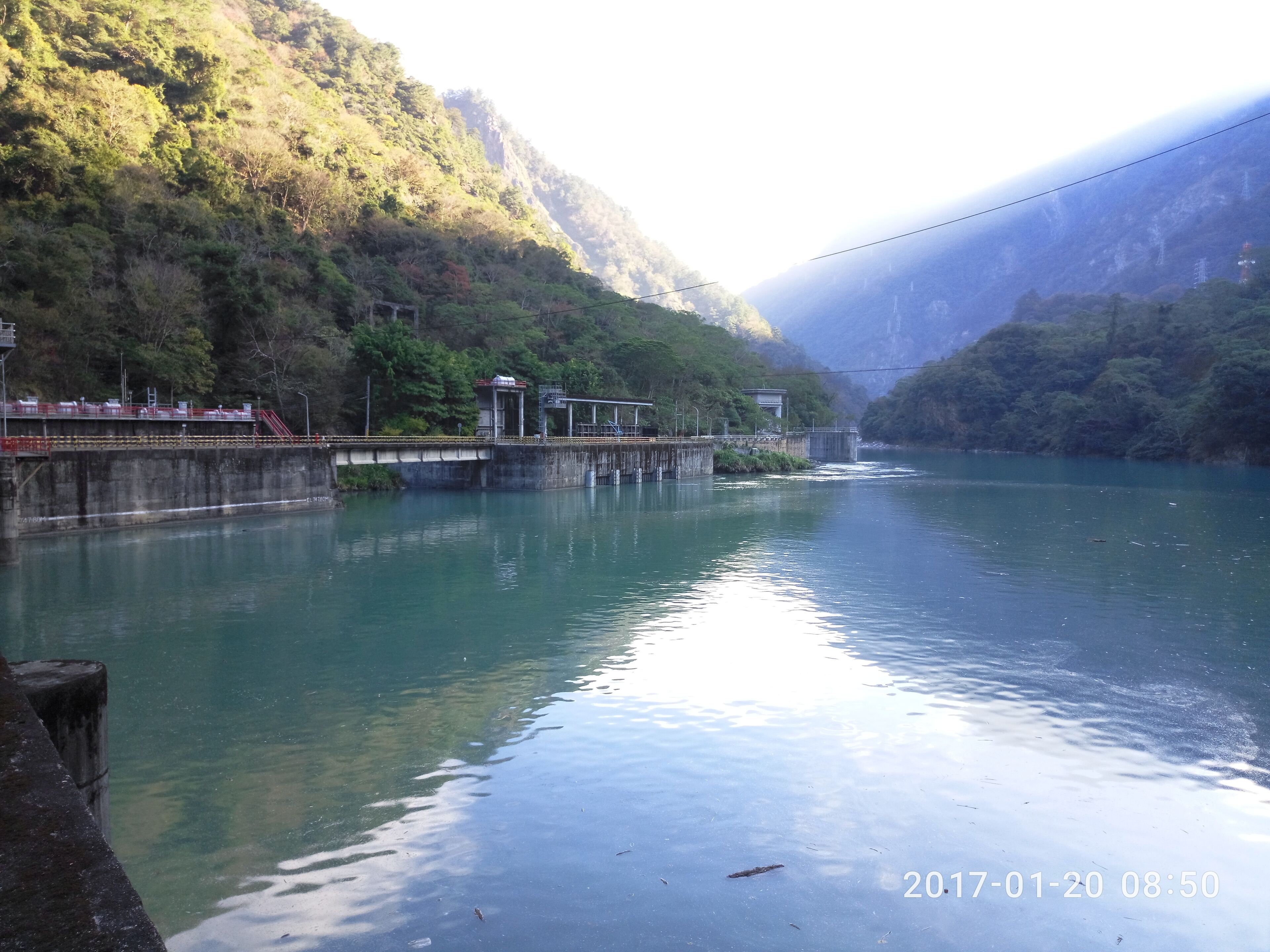Um rio calmo com uma ponte e uma barragem numa região montanhosa.