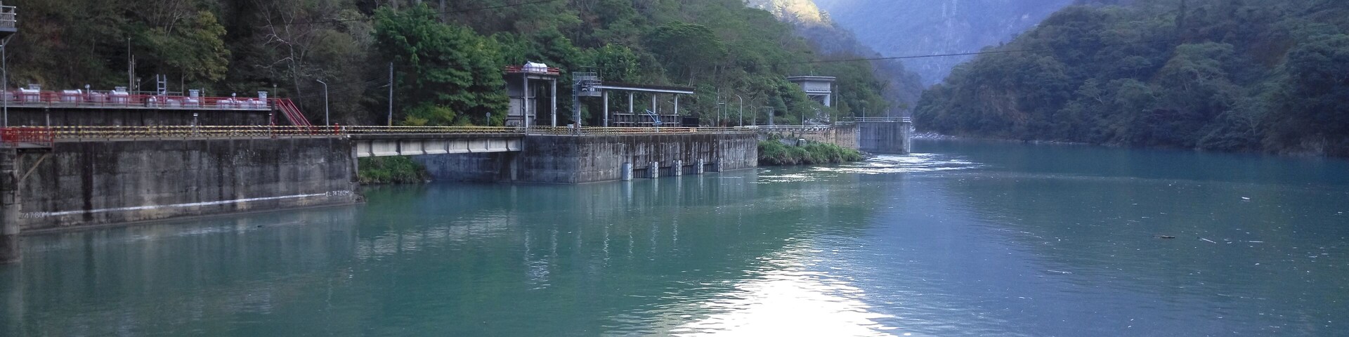 Um rio calmo com uma ponte e uma barragem numa região montanhosa.