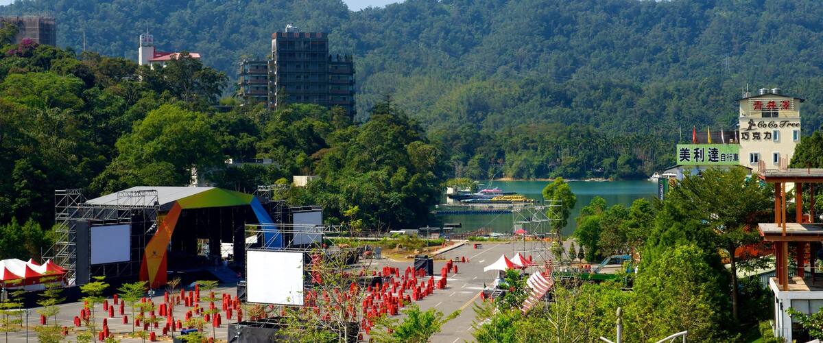 A scenic view of a mountainous area with a lake, a stage with a large screen, and a building with signage.