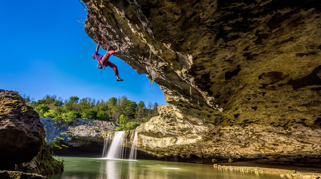 A person rock climbing a cliff with a waterfall in the background.