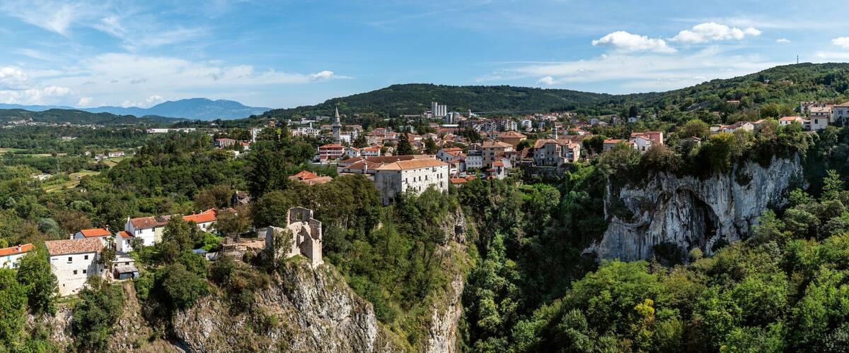 A town nestled in a valley with a prominent church and castle ruins on a cliff.
