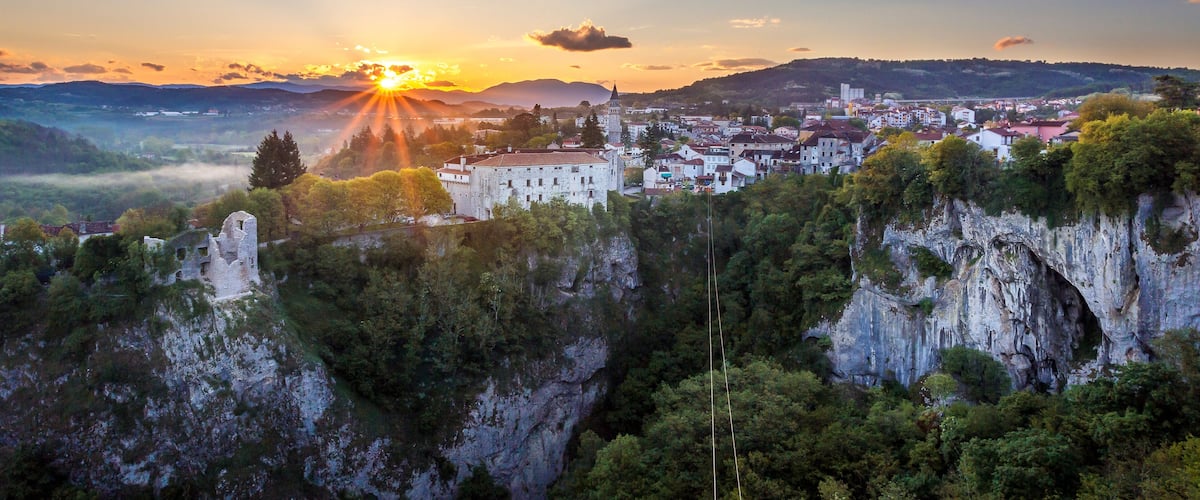 A sunset over a town nestled in a valley with a prominent cliff and a historic building.