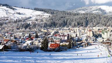 A snow-covered town with buildings, a ski slope, and a forested mountain in the background.