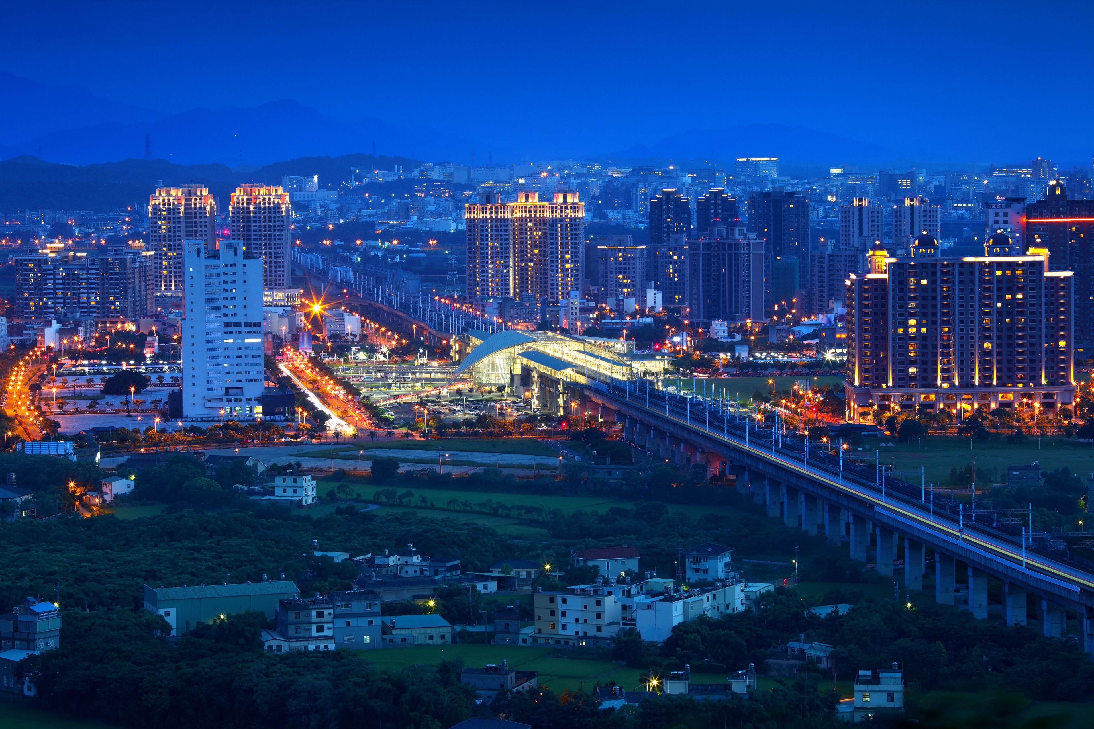 A cityscape at dusk with illuminated buildings and a bridge.