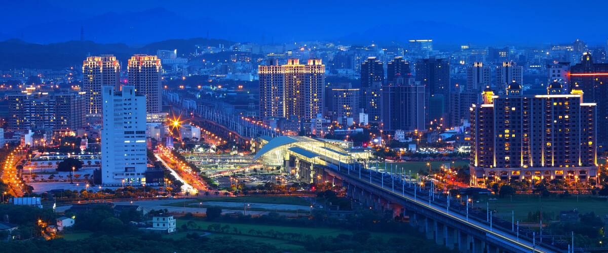 A cityscape at dusk with illuminated buildings and a bridge.