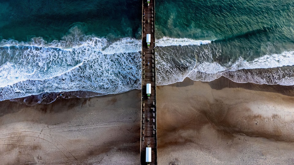 A coastal beach with a wooden pier extending into the ocean.