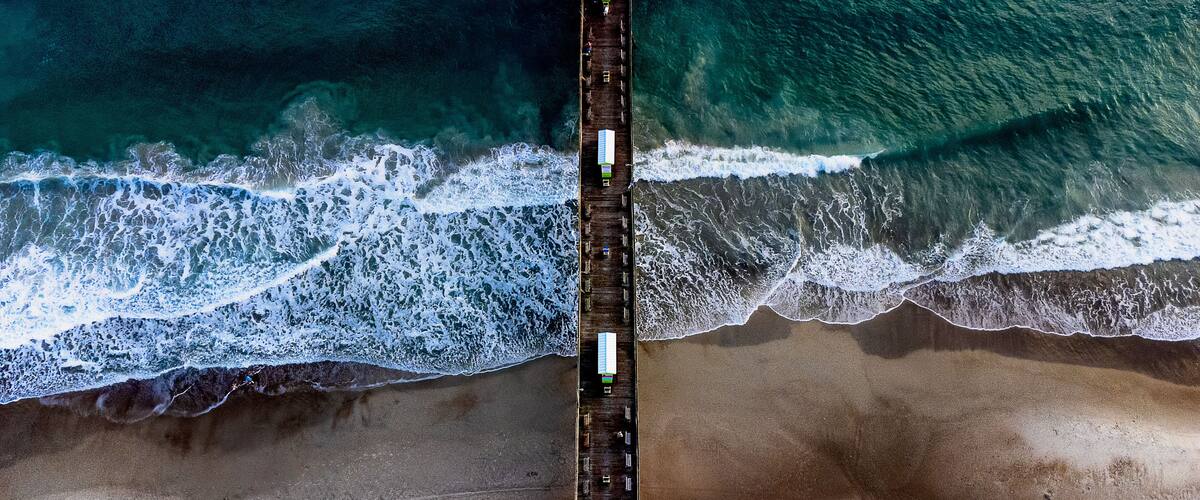 A coastal beach with a wooden pier extending into the ocean.