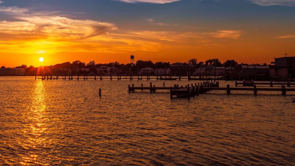 A sunset over a calm body of water with a pier extending into the water, surrounded by buildings.