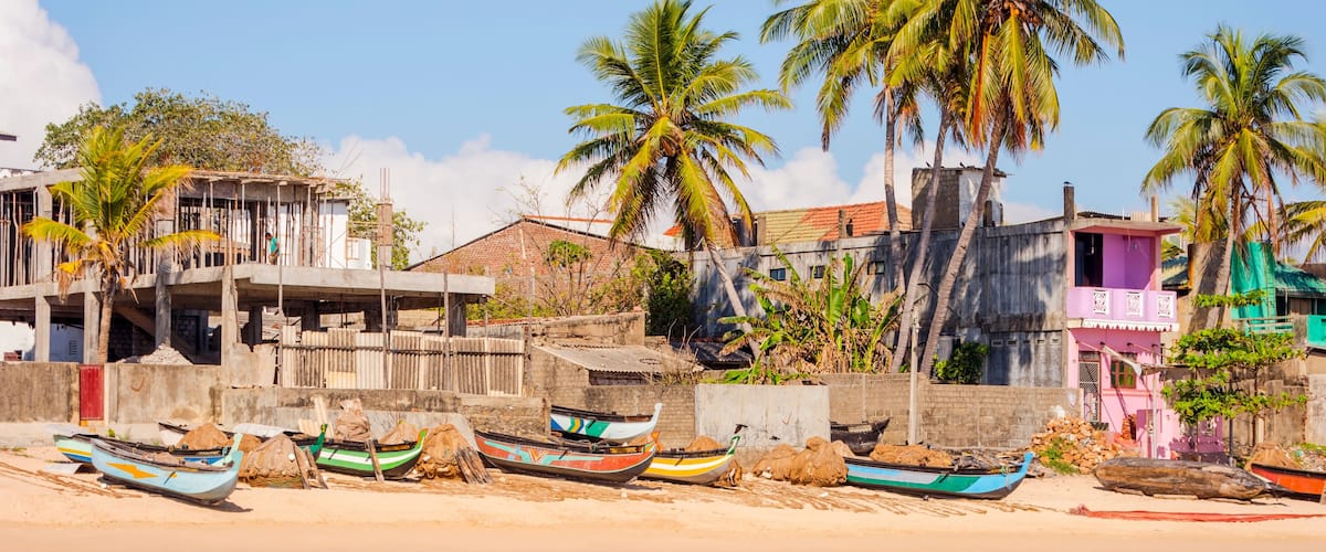 A beach with several boats, palm trees, and colorful buildings.