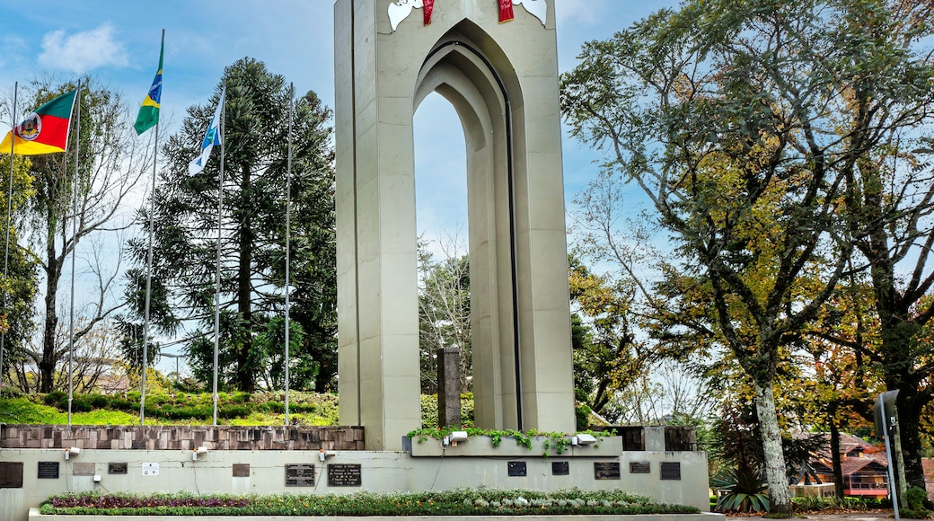 Um monumento alto com arcos, rodeado por árvores e bandeiras.