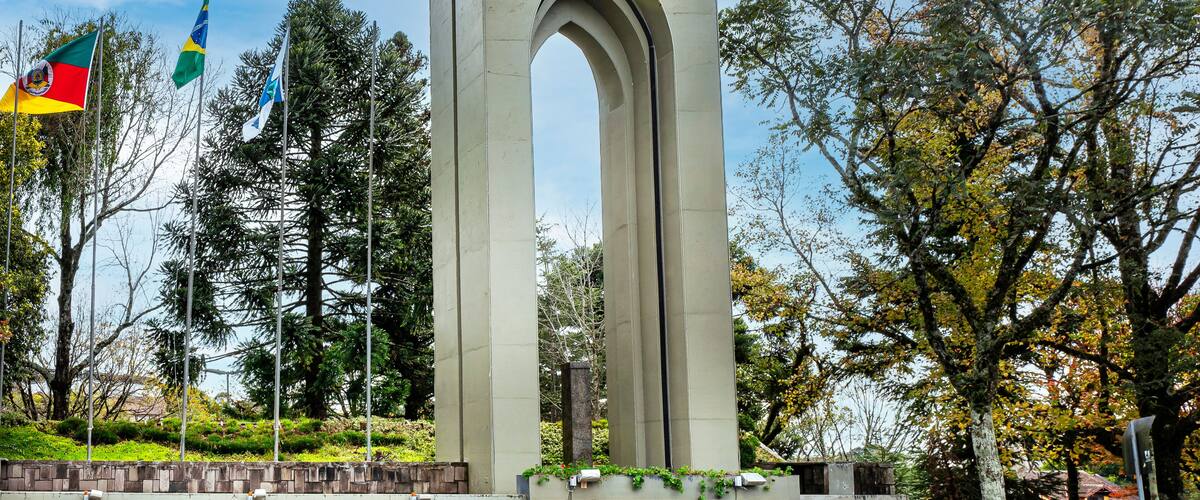 A tall monument with arches, surrounded by trees and flags.