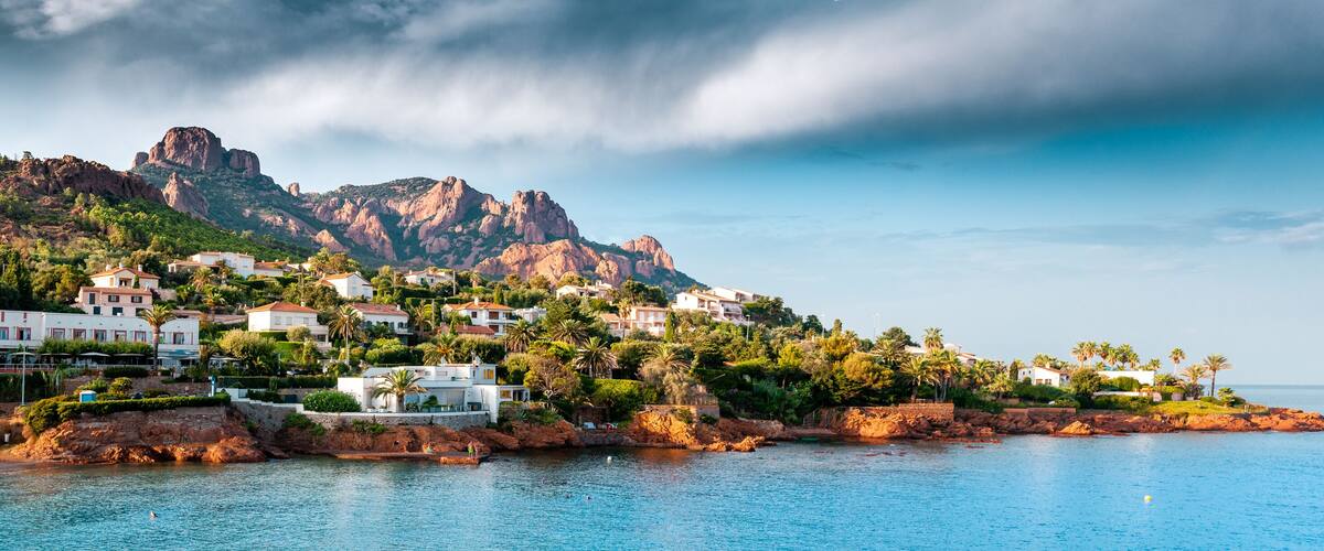 A coastal town with white houses, palm trees, and a rocky mountain in the background.