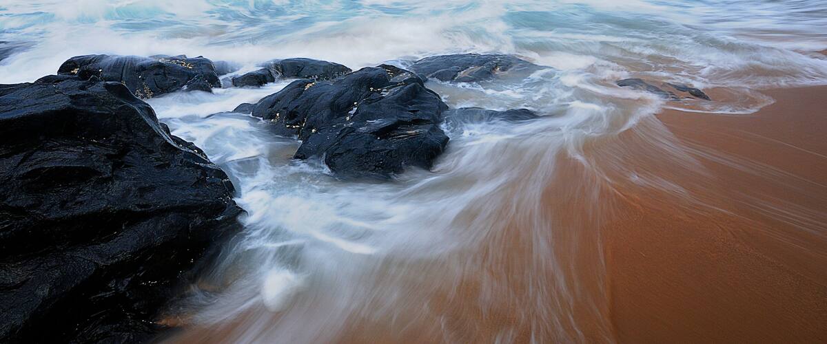 A beach with waves crashing against large rocks and a clear blue sky.