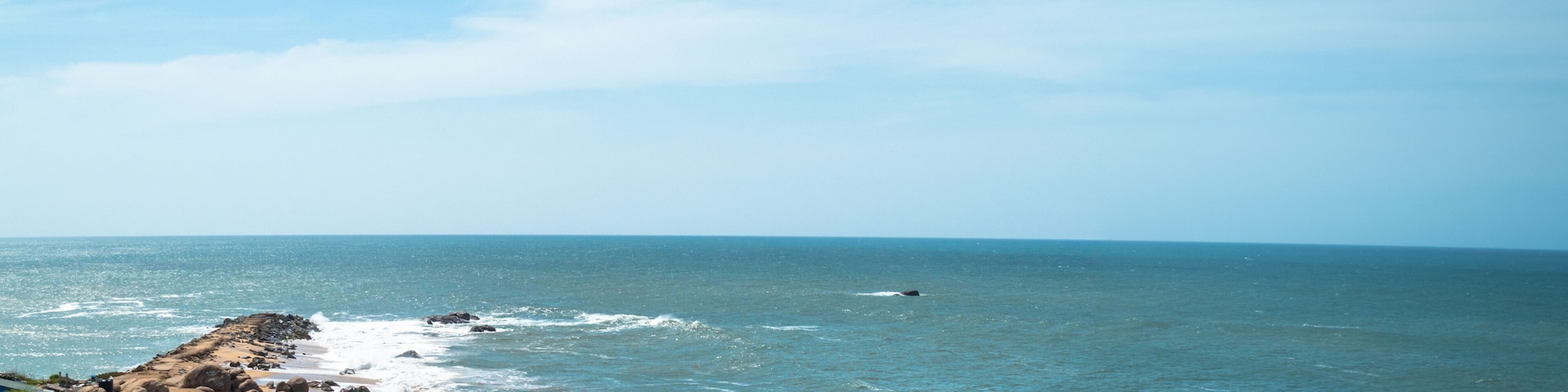 Una costa rocosa con olas rompiendo sobre la orilla bajo un cielo despejado.