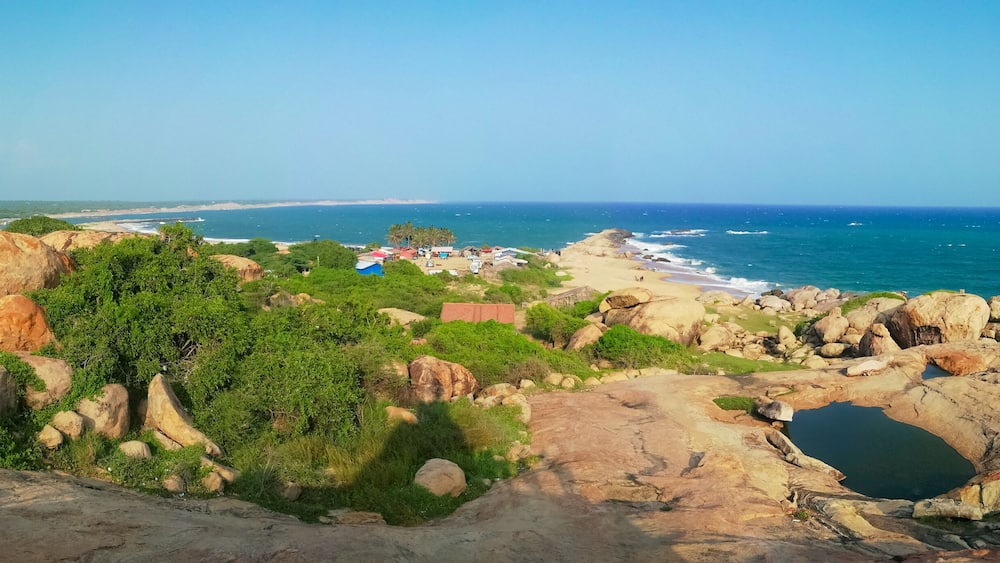A coastal landscape with rocky outcrops, greenery, and a beach in the distance.