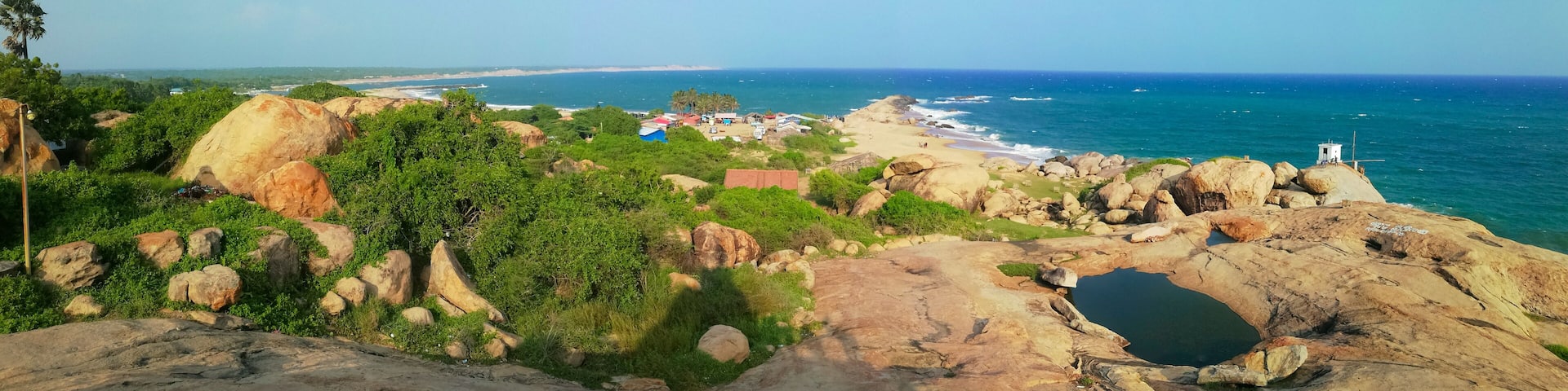 A coastal landscape with rocky outcrops, greenery, and a beach in the distance.