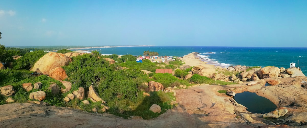 A coastal landscape with rocky outcrops, greenery, and a beach in the distance.