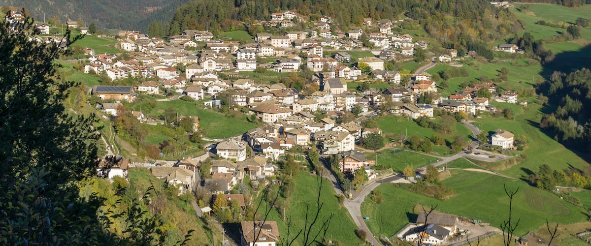 Un village de montagne où les maisons sont nichées dans la vallée, entouré de collines boisées et de sommets enneigés.