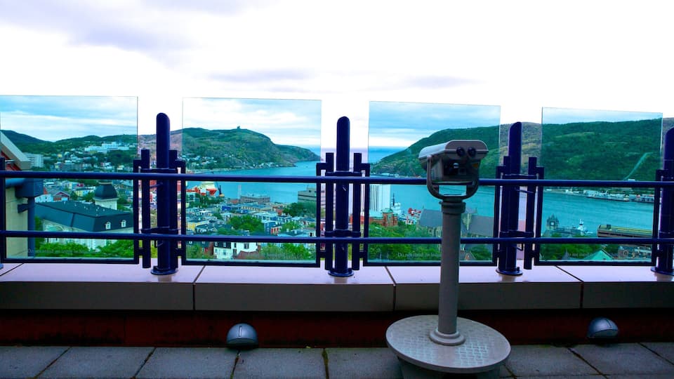 A pair of binoculars on a railing overlooking a coastal town with buildings and hills.