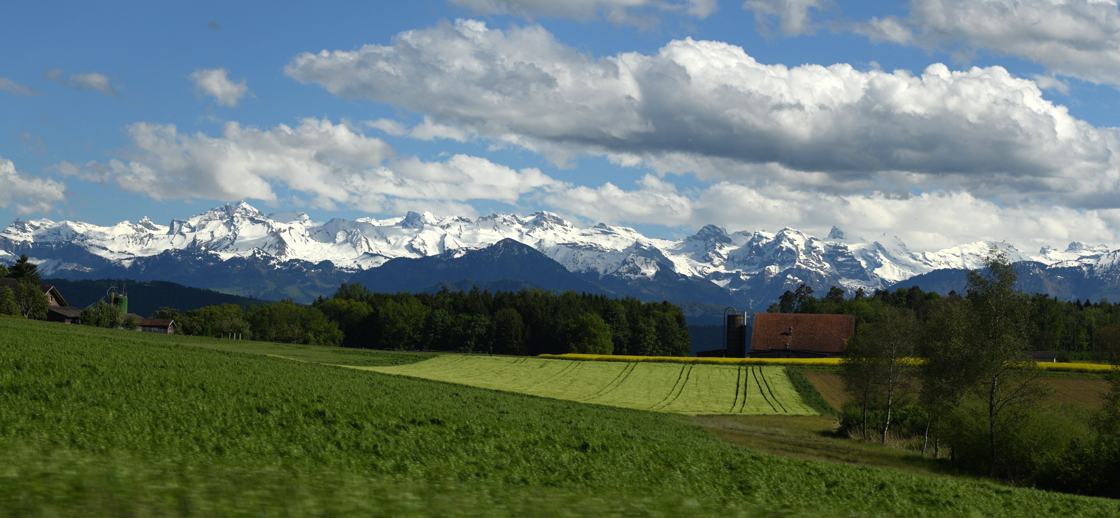 A green field, a red barn, and snow-capped mountains under a blue sky.