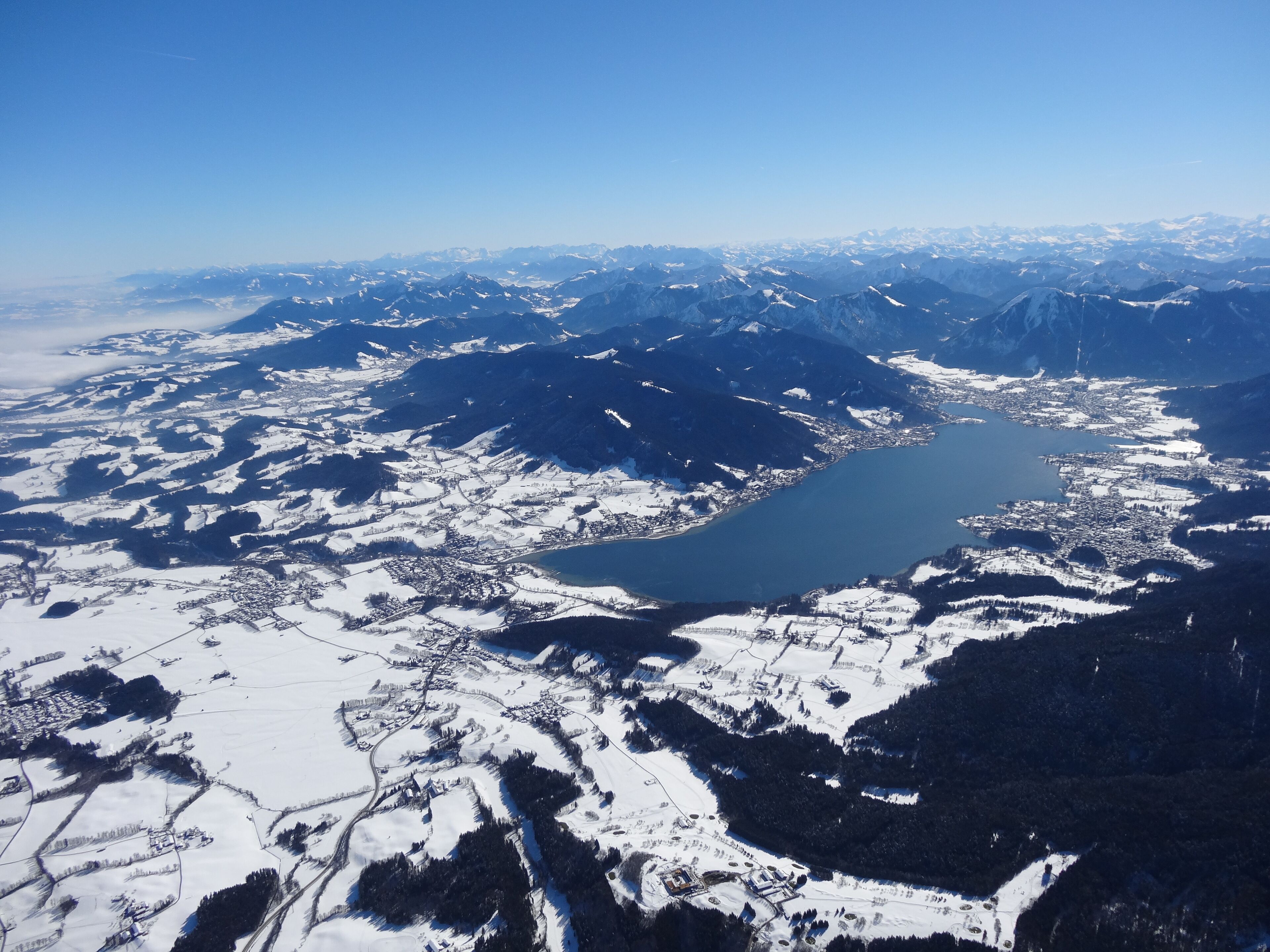 A snow-covered mountainous landscape with a lake and a town.