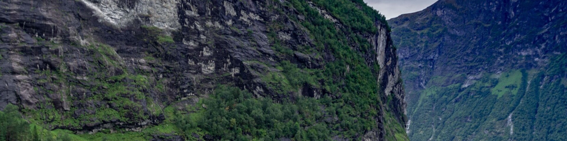 Una barca en un lago tranquilo rodeada de acantilados cubiertos de bosque.