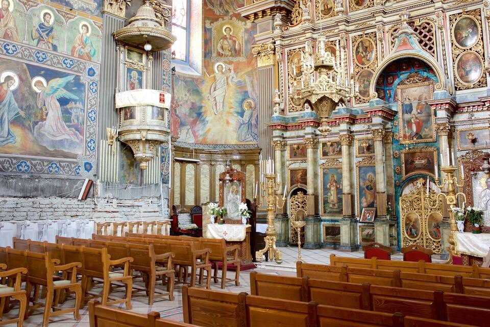 Interior de una iglesia ornamentada con pinturas religiosas, candelabros dorados y bancales de madera.