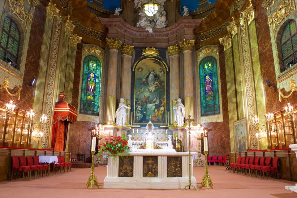 An ornate church interior with a central altar, stained glass windows, and statues.