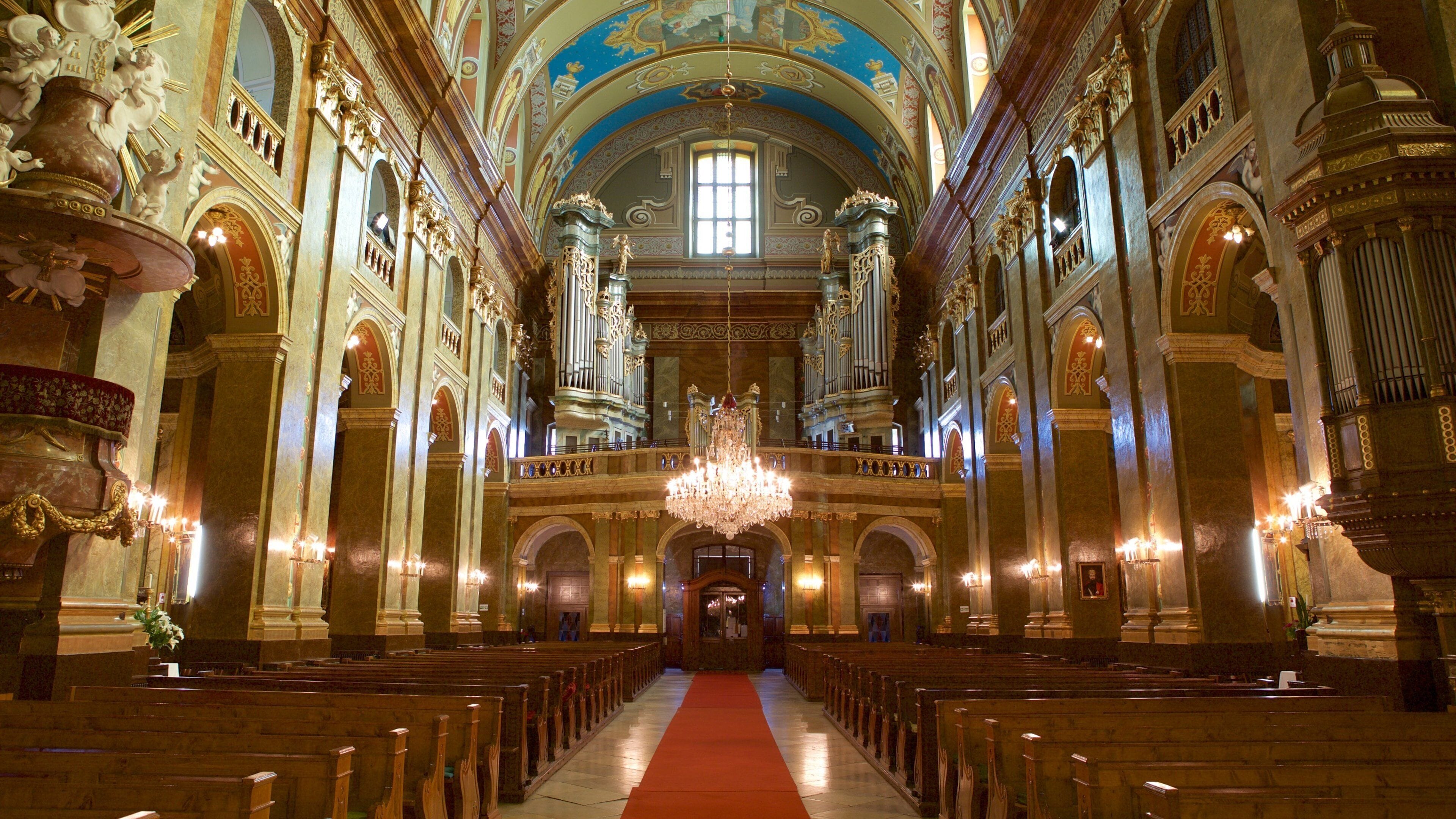 Interior de iglesia ornamentado, con pasillo de alfombra roja, candelabros dorados y frescos detallados en el techo.