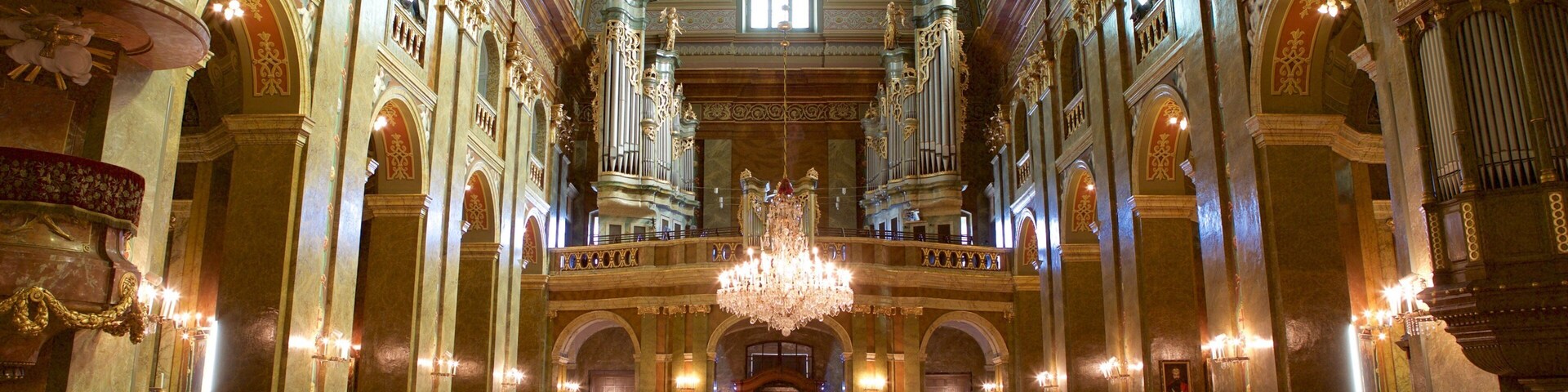 Interior de iglesia ornamentado, con pasillo de alfombra roja, candelabros dorados y frescos detallados en el techo.