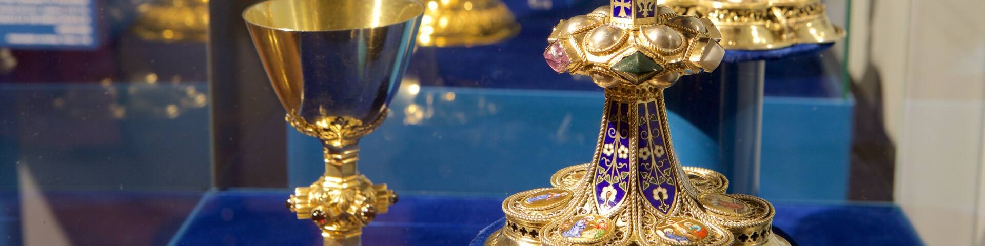 A display of ornate religious artifacts, including a golden chalice and a decorated paten, on a blue velvet cloth.