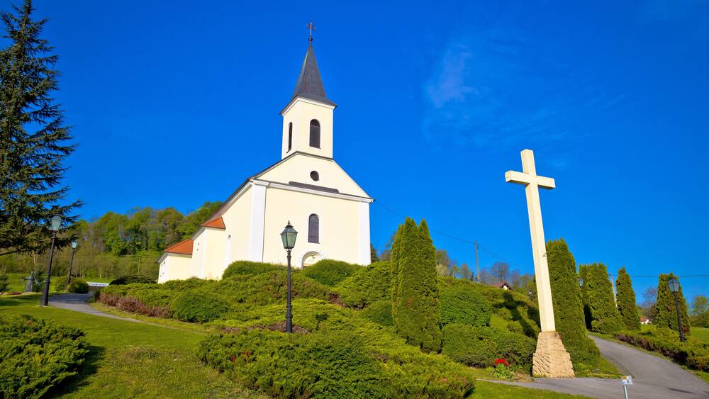A church with a tall steeple and a large cross in front.