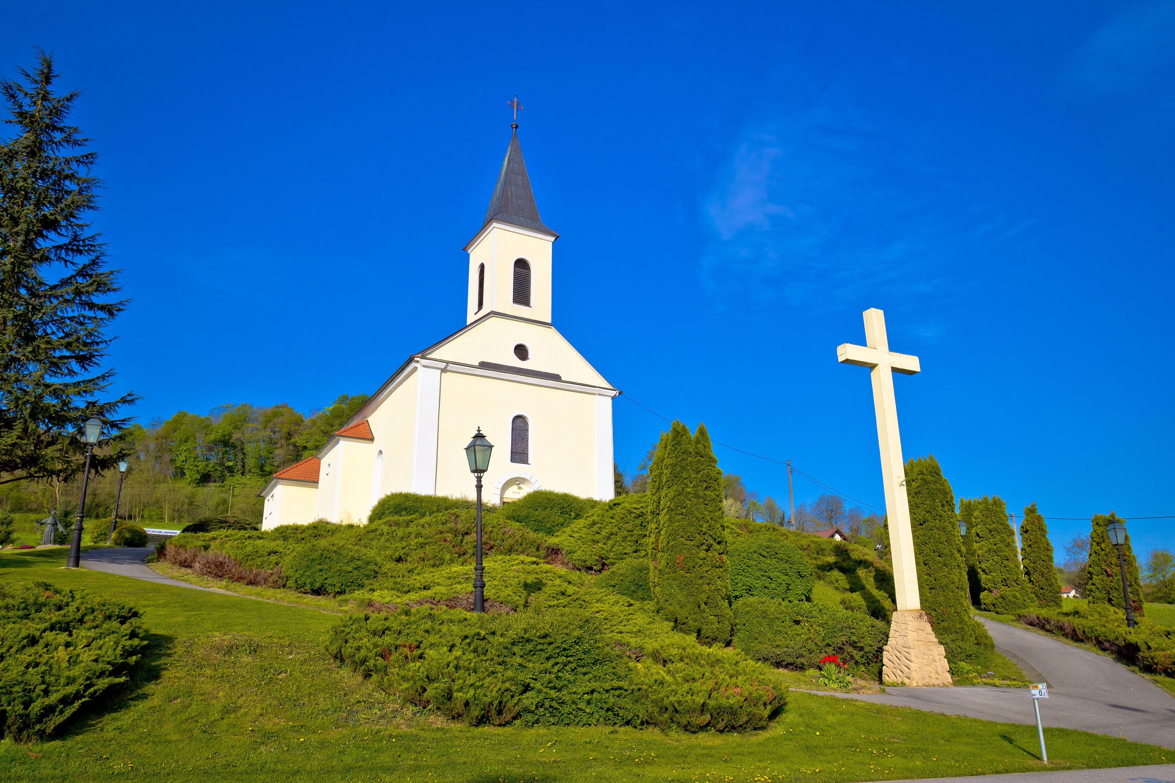 A church with a tall steeple and a large cross in front.
