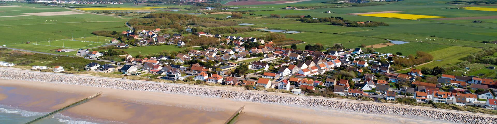 A coastal village with houses, a beach, and fields.
