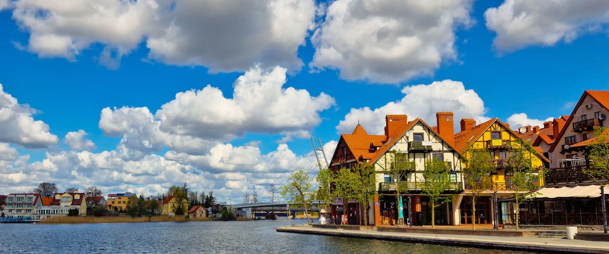 A riverside town with colorful buildings and a bridge in the background.